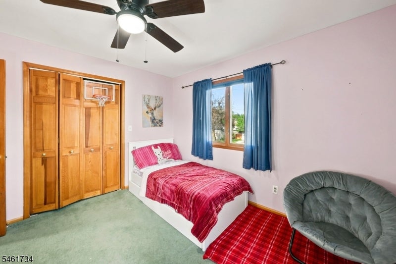 Bedroom with a red-covered bed, wooden closet doors with a basketball hoop, and a window framed by blue curtains.