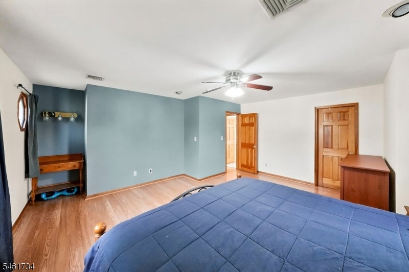 Bedroom with a large blue bed, blue accent walls, light wood floors, and a ceiling fan.