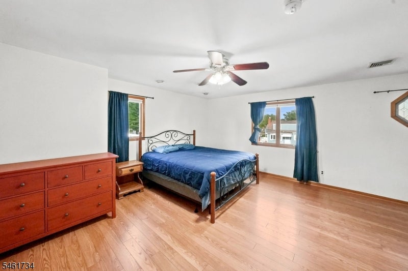 Furnished bedroom with blue bedding, a metal bed frame, hardwood floors, and a ceiling fan.