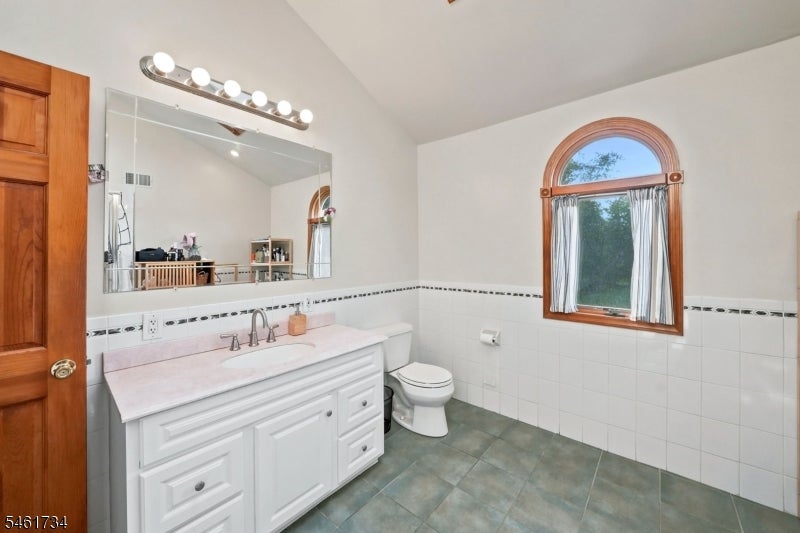 Bathroom with a white vanity, tiled walls, and an arched wood-framed window.
