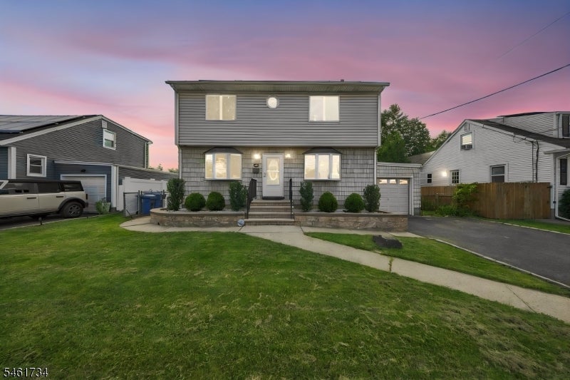 Two-story gray-sided house with a curved front walk and lawn at dusk.