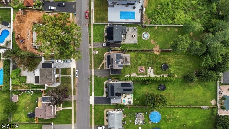 Aerial view of a residential street with green yards, trees, and swimming pools.