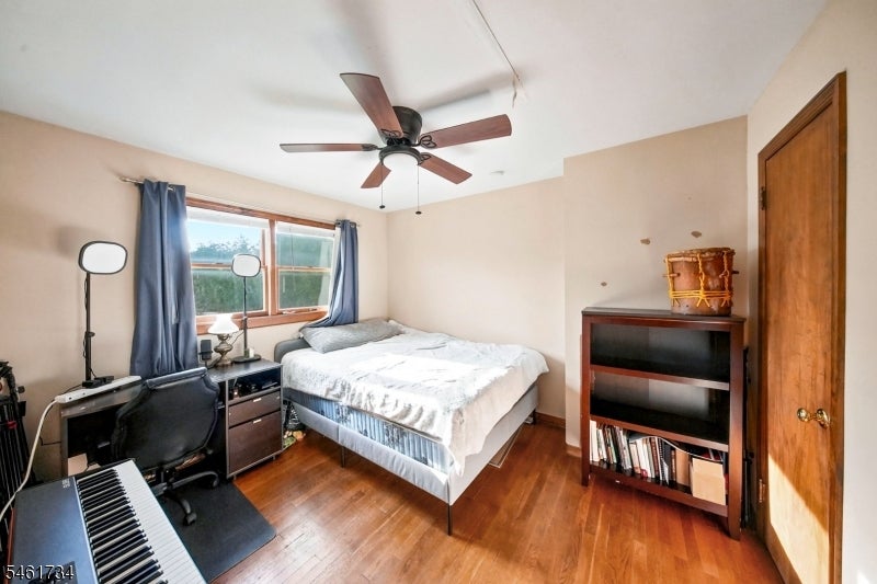 Bedroom with a bed, ceiling fan, blue curtains, and a desk with a keyboard.