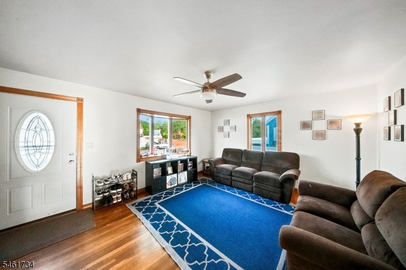 Living room with brown sofas, a bright blue patterned rug, hardwood floors, and a ceiling fan.
