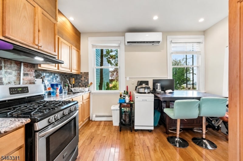 Kitchen with exposed brick backsplash, stainless steel range, and dining table beside two windows.