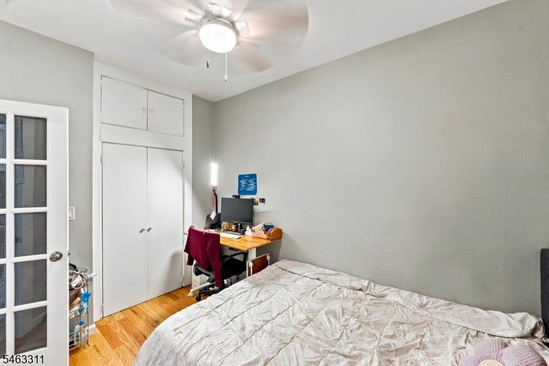 Bedroom with a built-in closet, desk, hardwood floor, and ceiling fan.