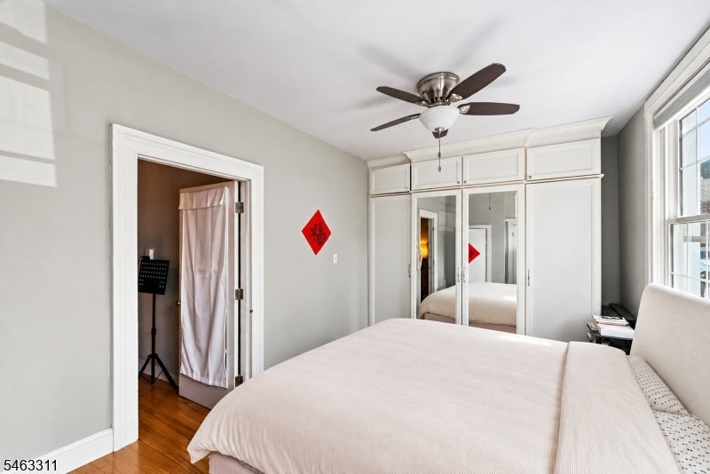 Bright bedroom with mirrored built-in wardrobes, a ceiling fan, and tall windows.