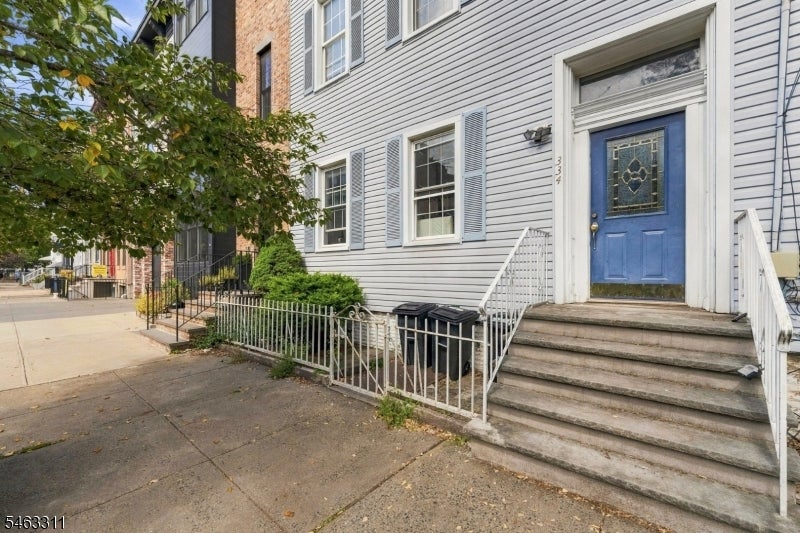 Gray-sided townhouse entrance with a blue door, broad stone steps, and white railings.
