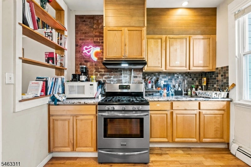Kitchen with honey-colored cabinets, stainless-steel range, exposed brick, and open shelving.