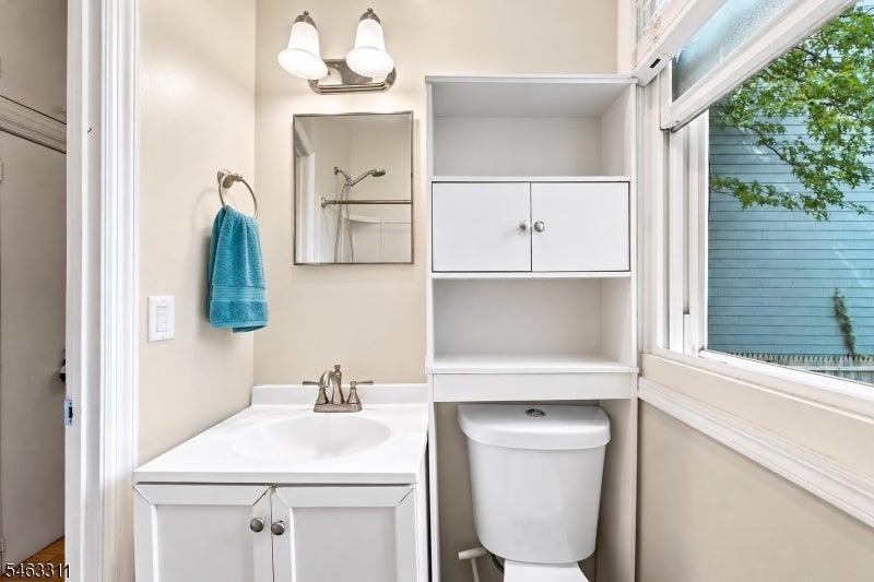 Bathroom with a white vanity and toilet beneath built-in storage beside a large window.