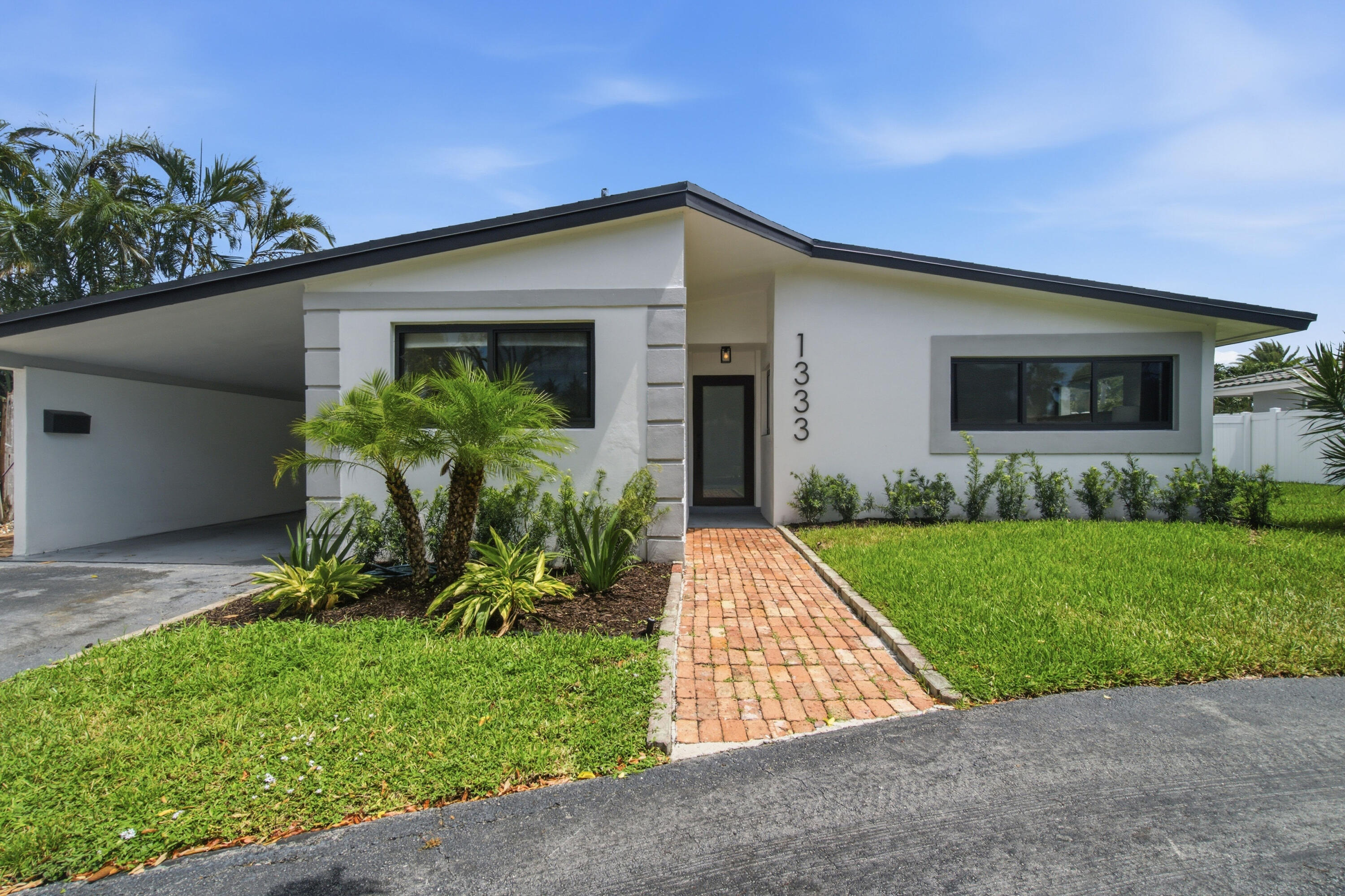 Modern white single-story home with a covered carport, palm landscaping, and brick front walkway.
