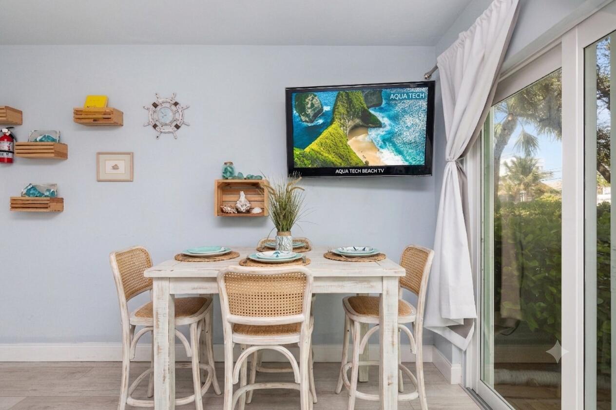 Dining area with a whitewashed table, woven chairs, coastal decor, and sliding glass doors.