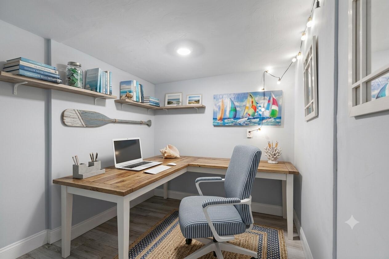 Furnished home office with an L-shaped wood desk, striped chair, and nautical wall art.