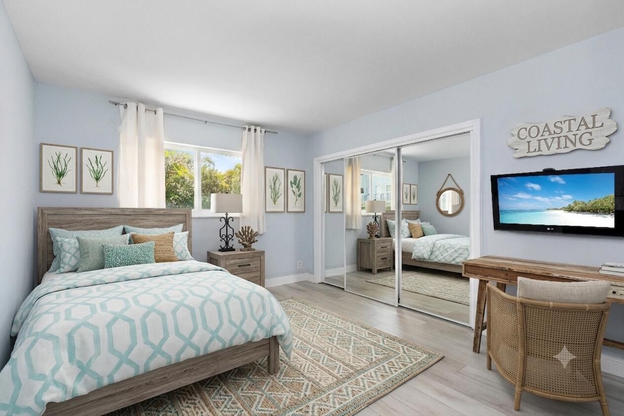 Coastal-style bedroom with aqua geometric bedding, mirrored closet doors, and a television showing a beach.