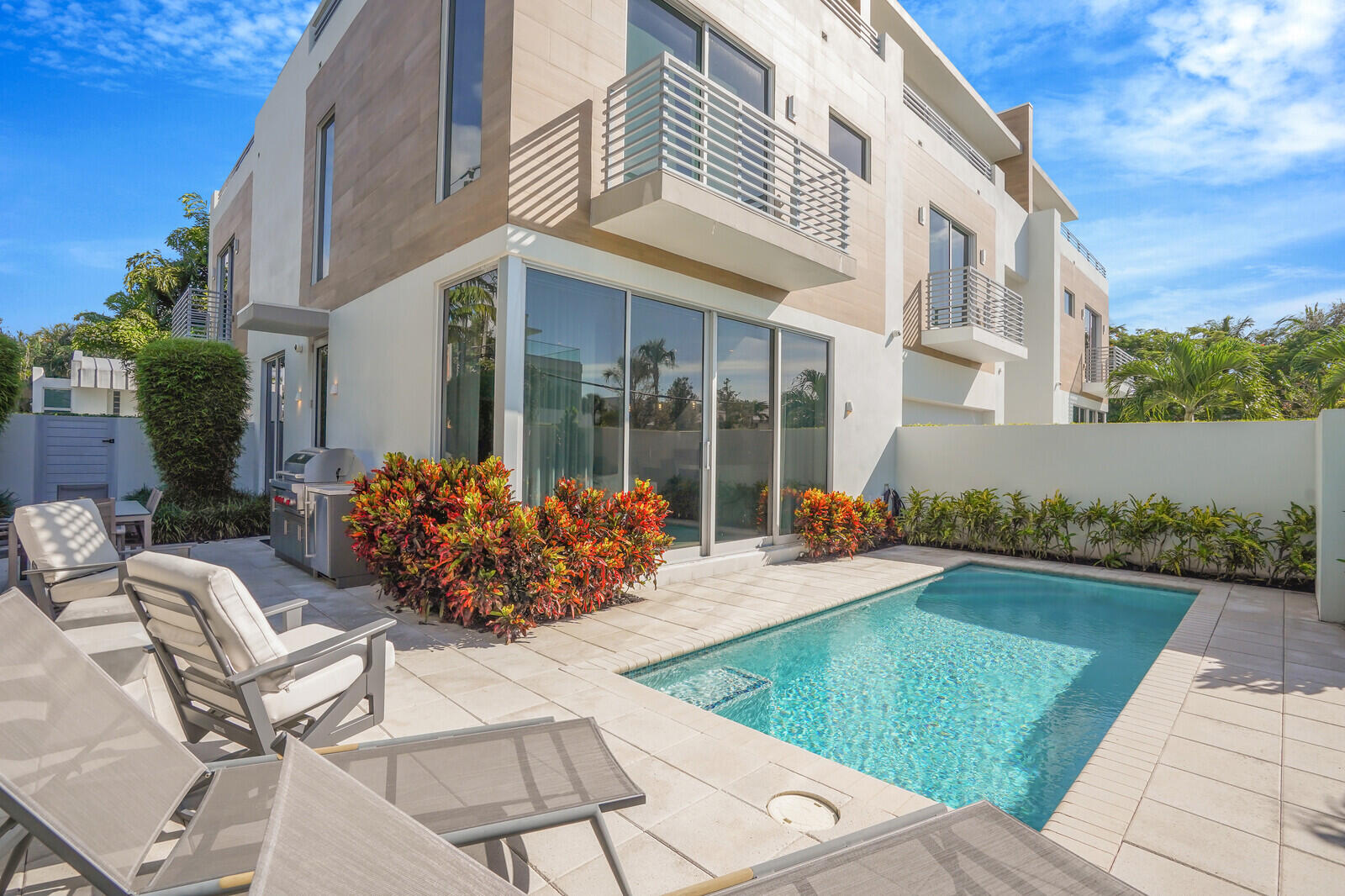 Modern home with balconies overlooking a backyard pool and furnished stone patio.
