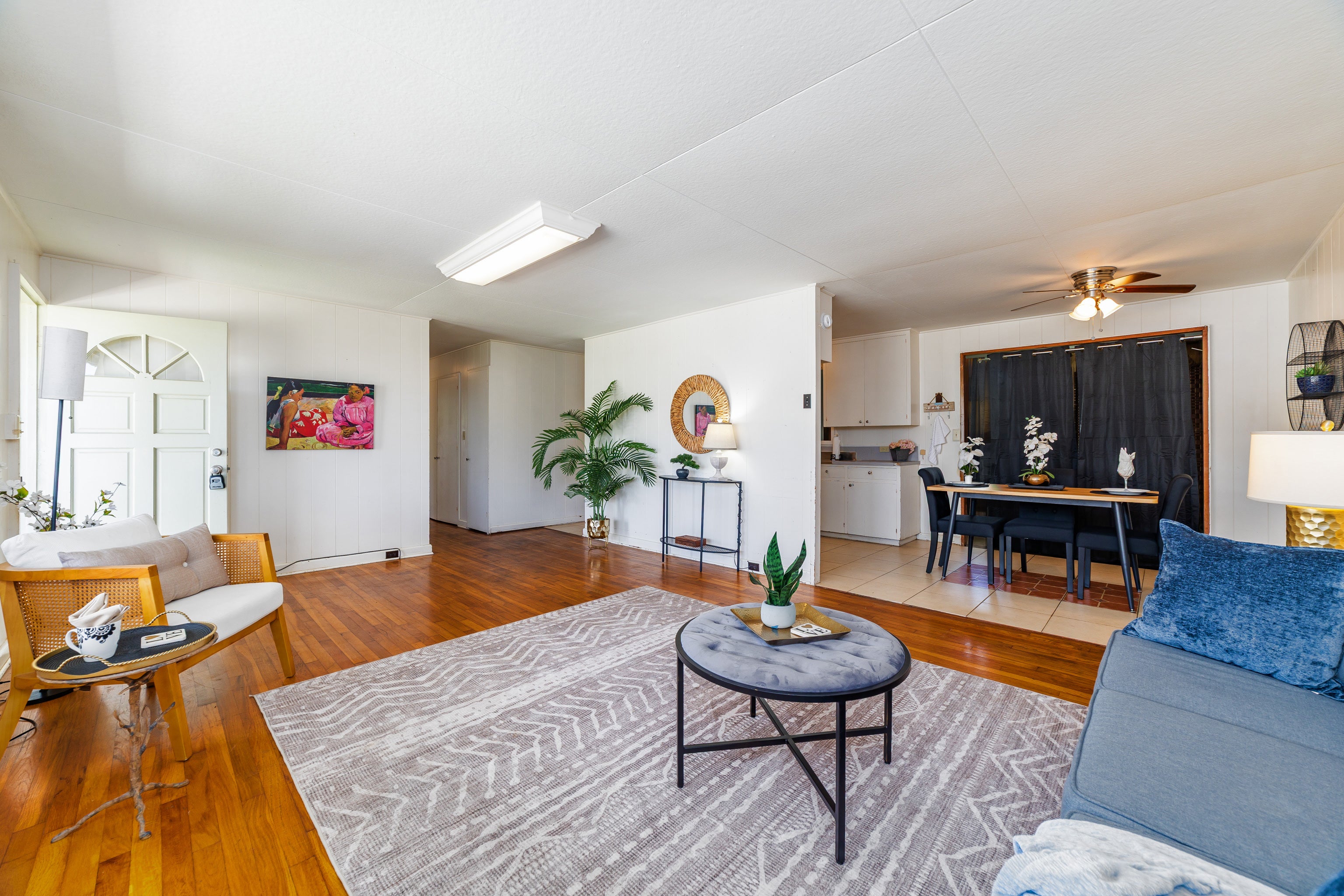 Open living and dining room with hardwood floors, a blue sofa, and a dining table beside the kitchen.