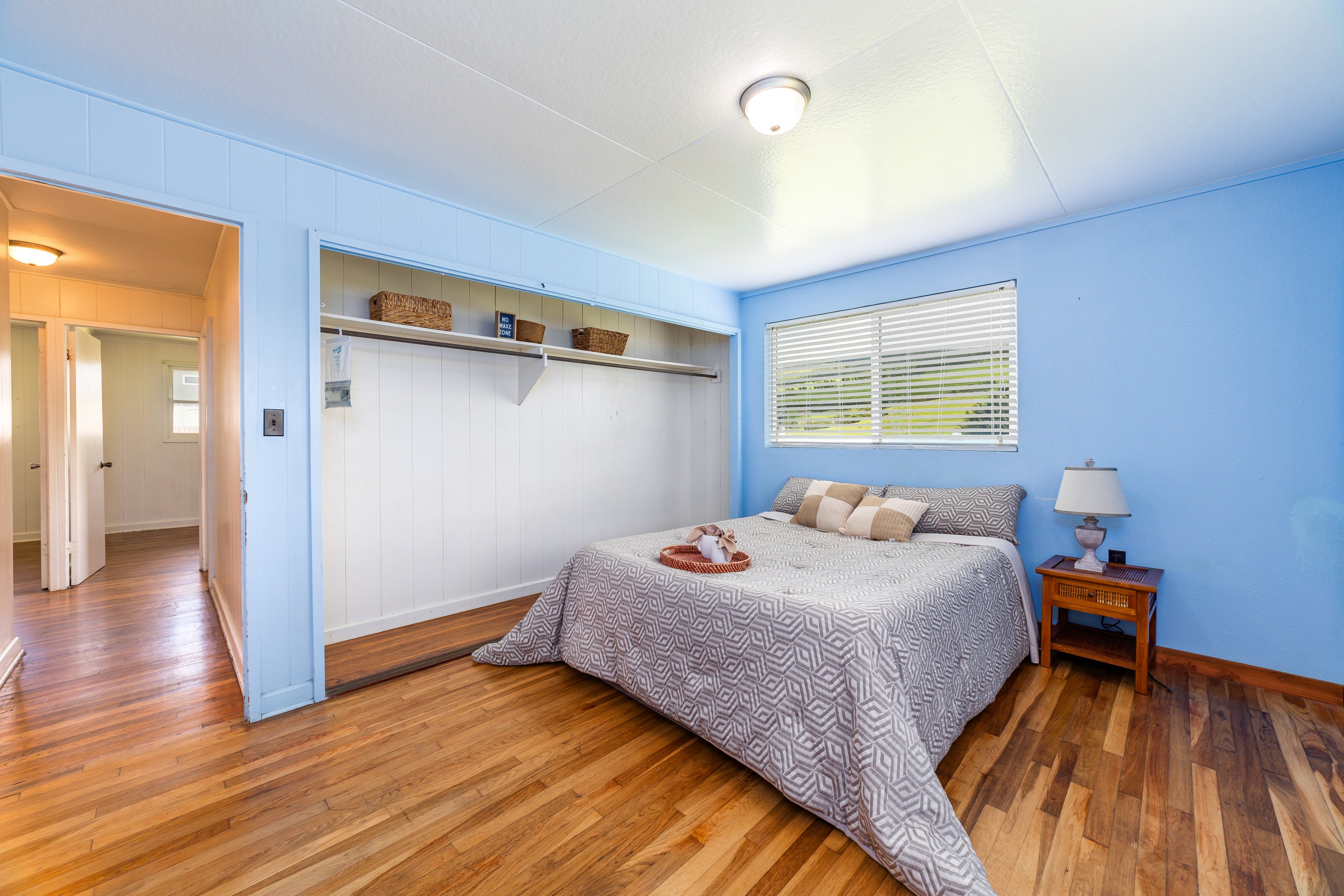 Bedroom with a geometric-patterned bed, blue walls, hardwood floors, and a wide built-in open closet.