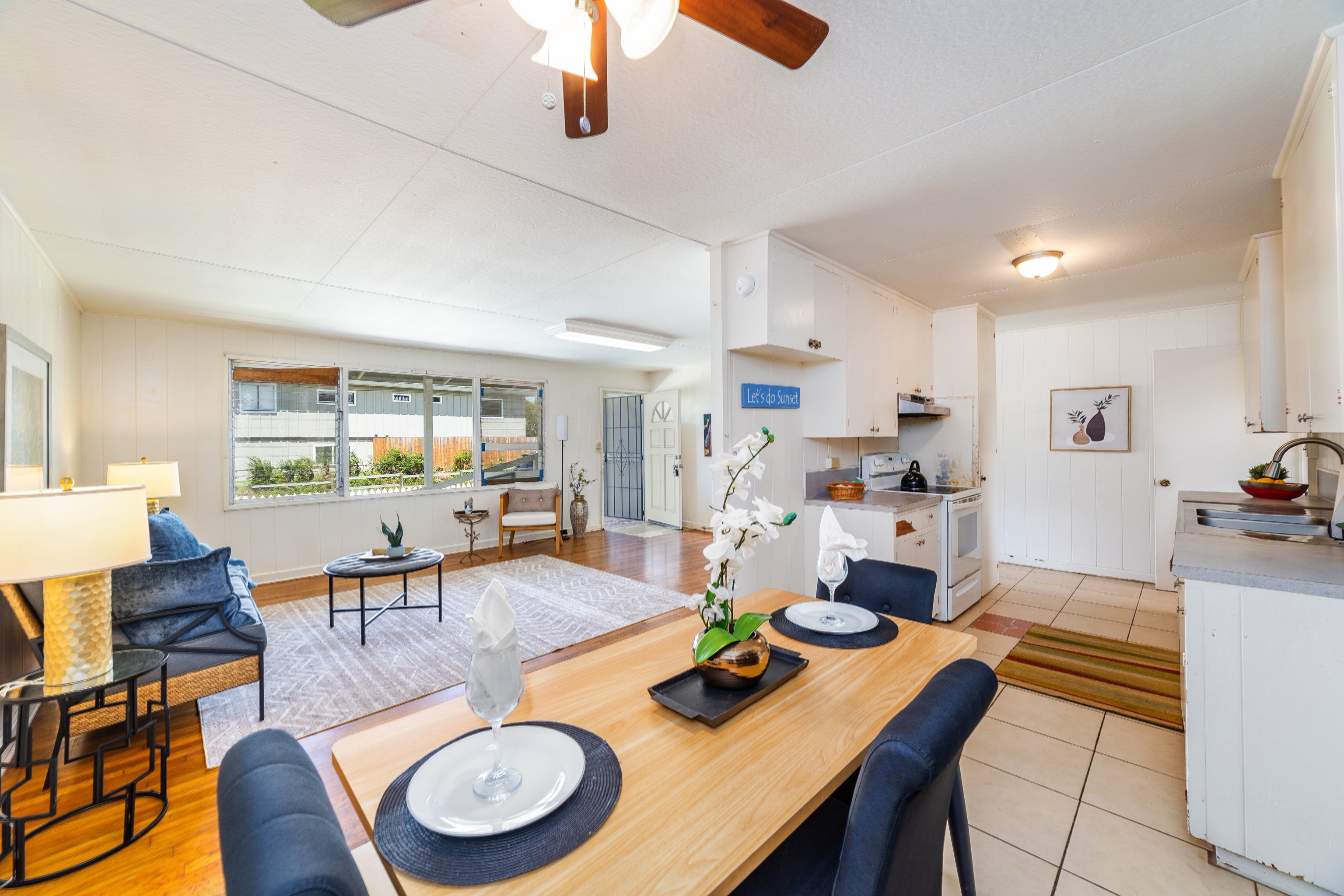 Open-plan living room and kitchen with a set dining table, blue seating, and large windows.