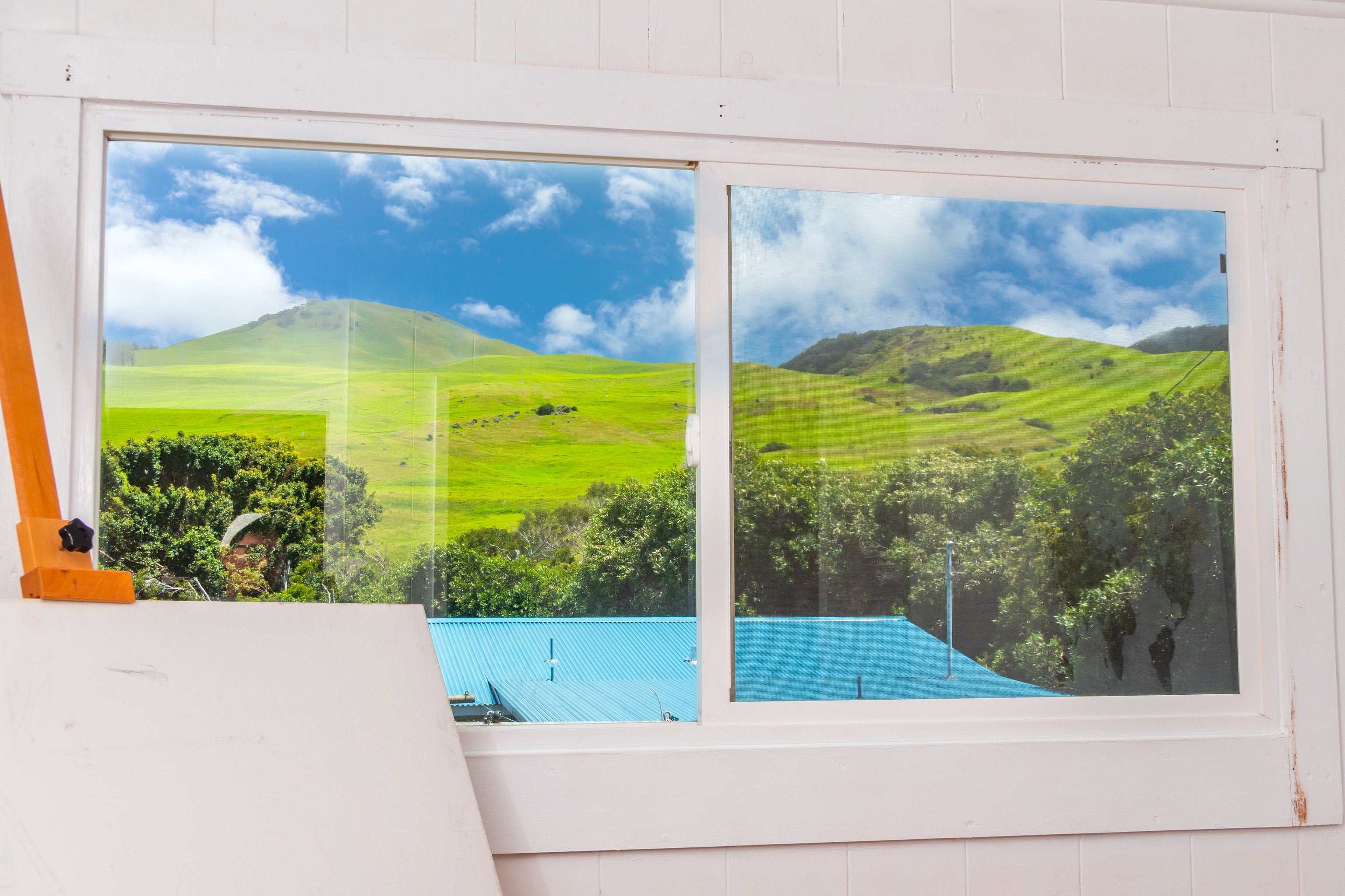 Rolling green hills and trees beyond a large sliding window, with a blue roof below.