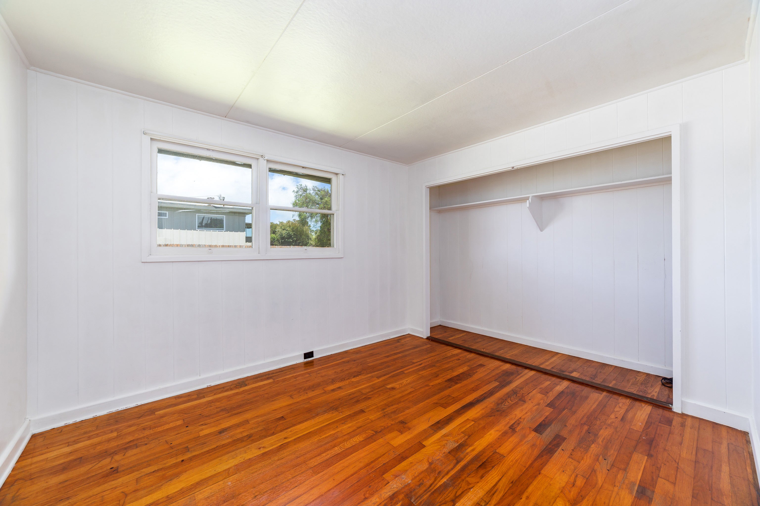 Vacant room with a built-in closet, paired windows, and reddish-brown hardwood floors.
