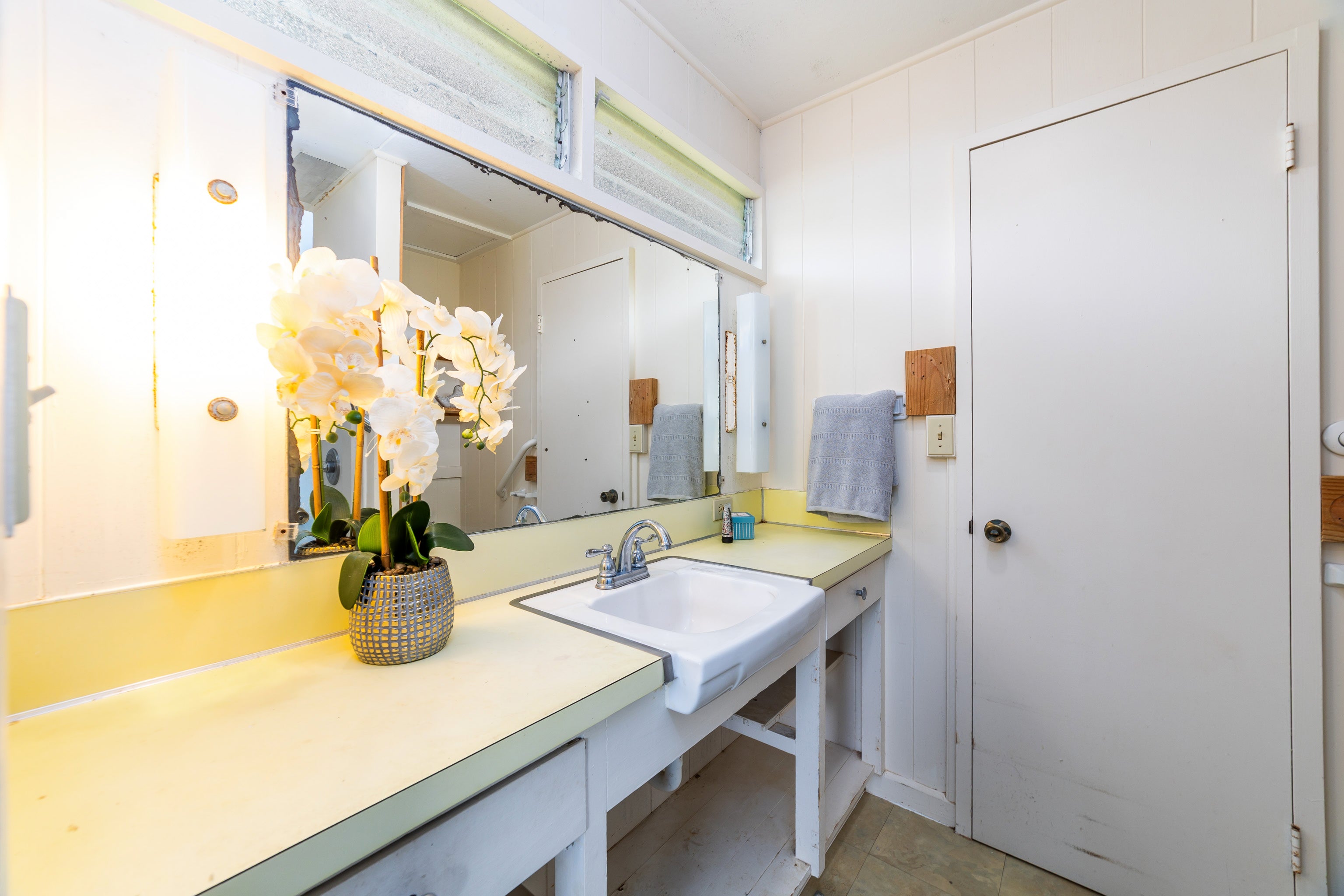 Bathroom vanity with a pale yellow counter, large mirror, and potted white orchid.