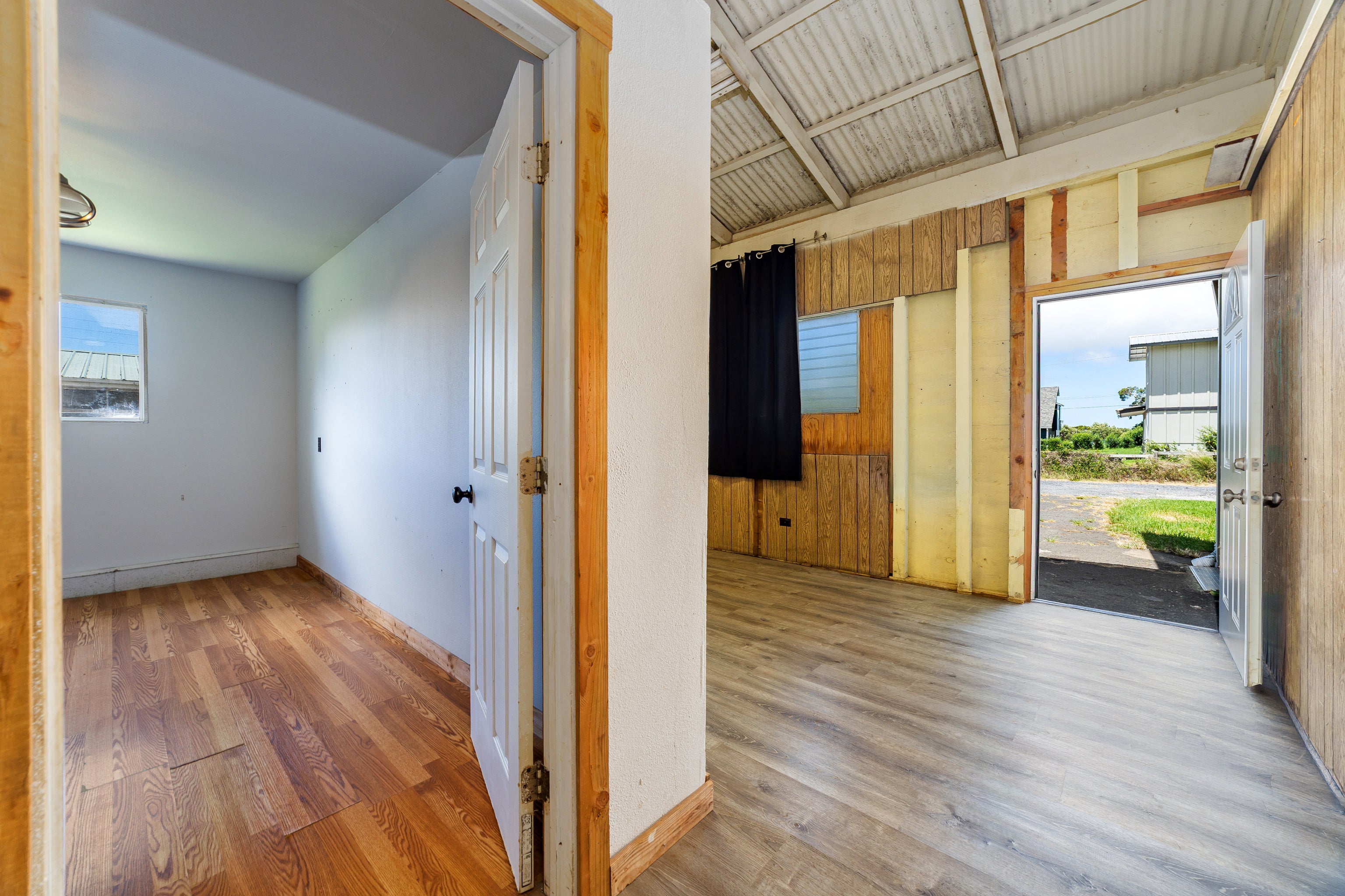 Two vacant rooms with wood-look floors, exposed framing, and an open door to the exterior.