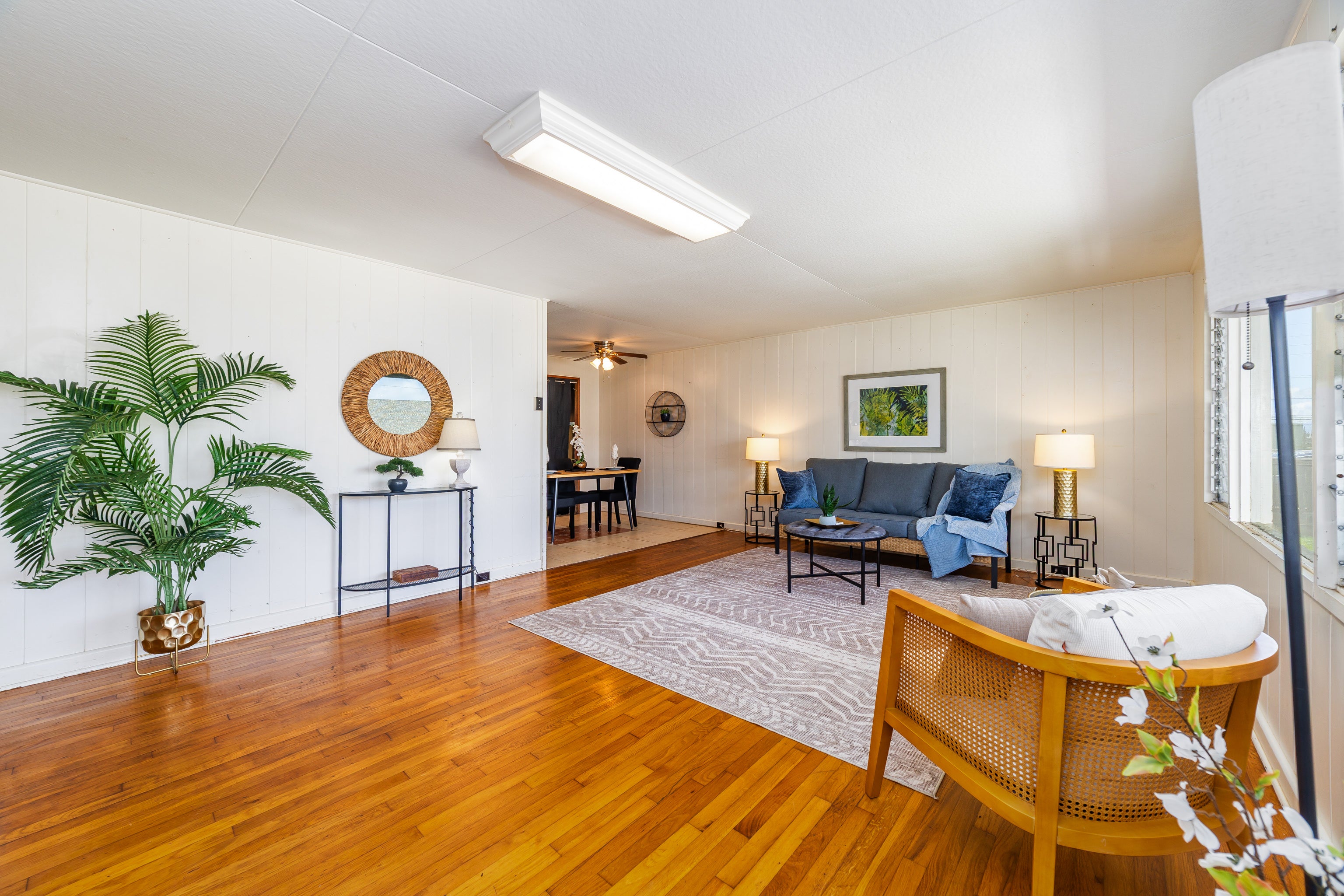 Staged living room with hardwood floors, gray sofa, patterned rug, and a view into the dining area.