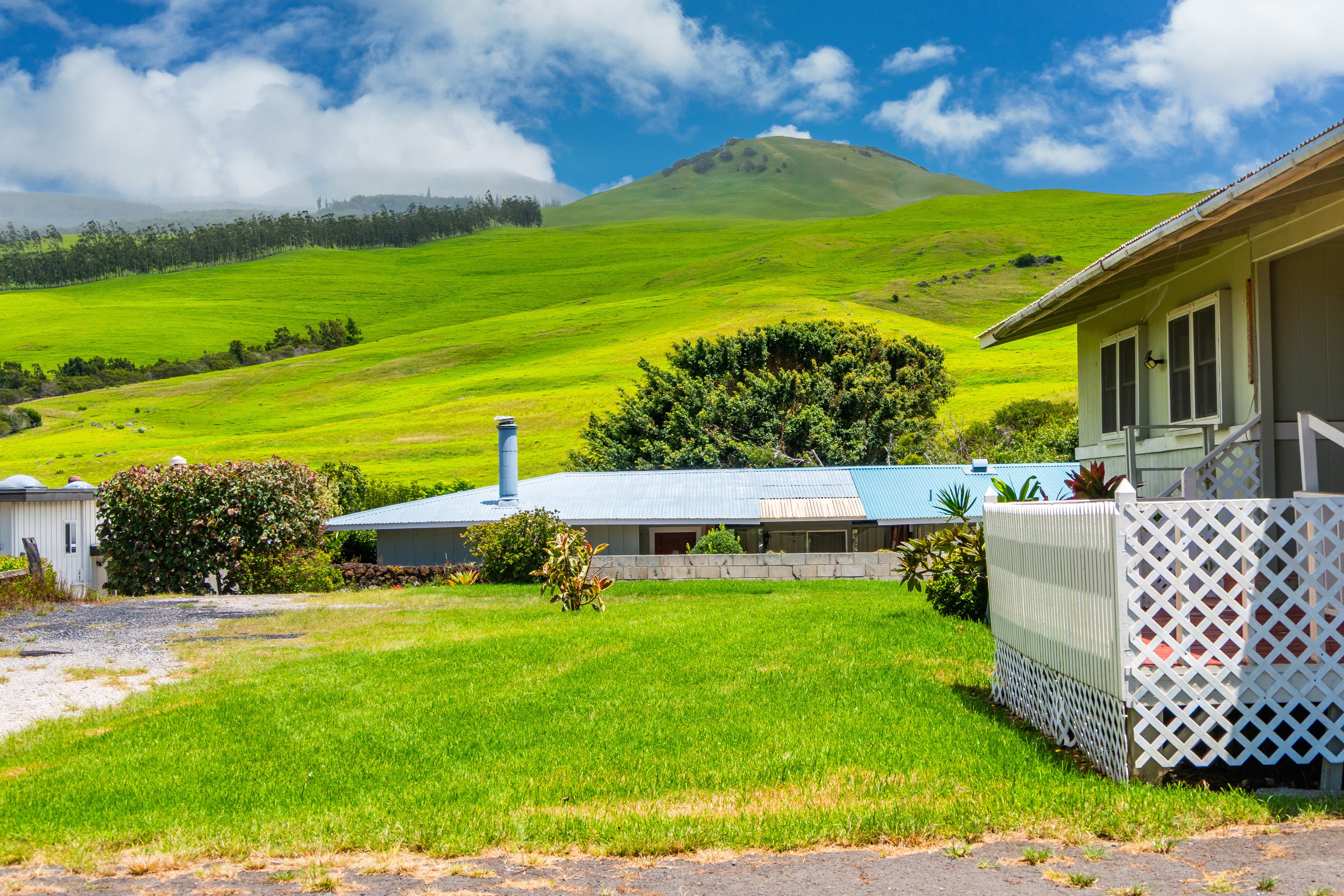 Property with a white lattice porch, broad lawn, and green mountain hills behind it.