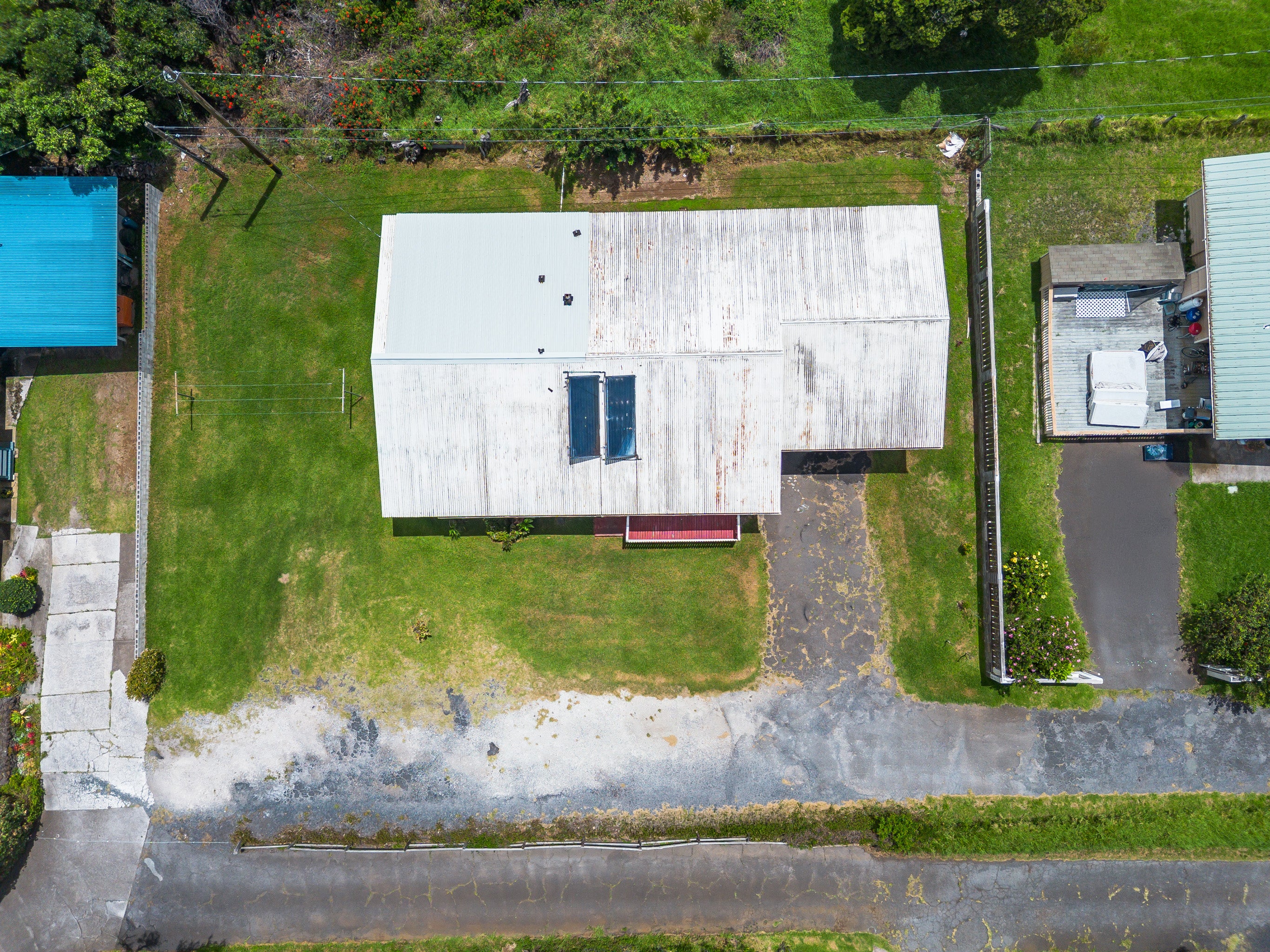 Aerial view of a metal-roofed home with solar water-heating panels, grassy yard, and paved driveway.