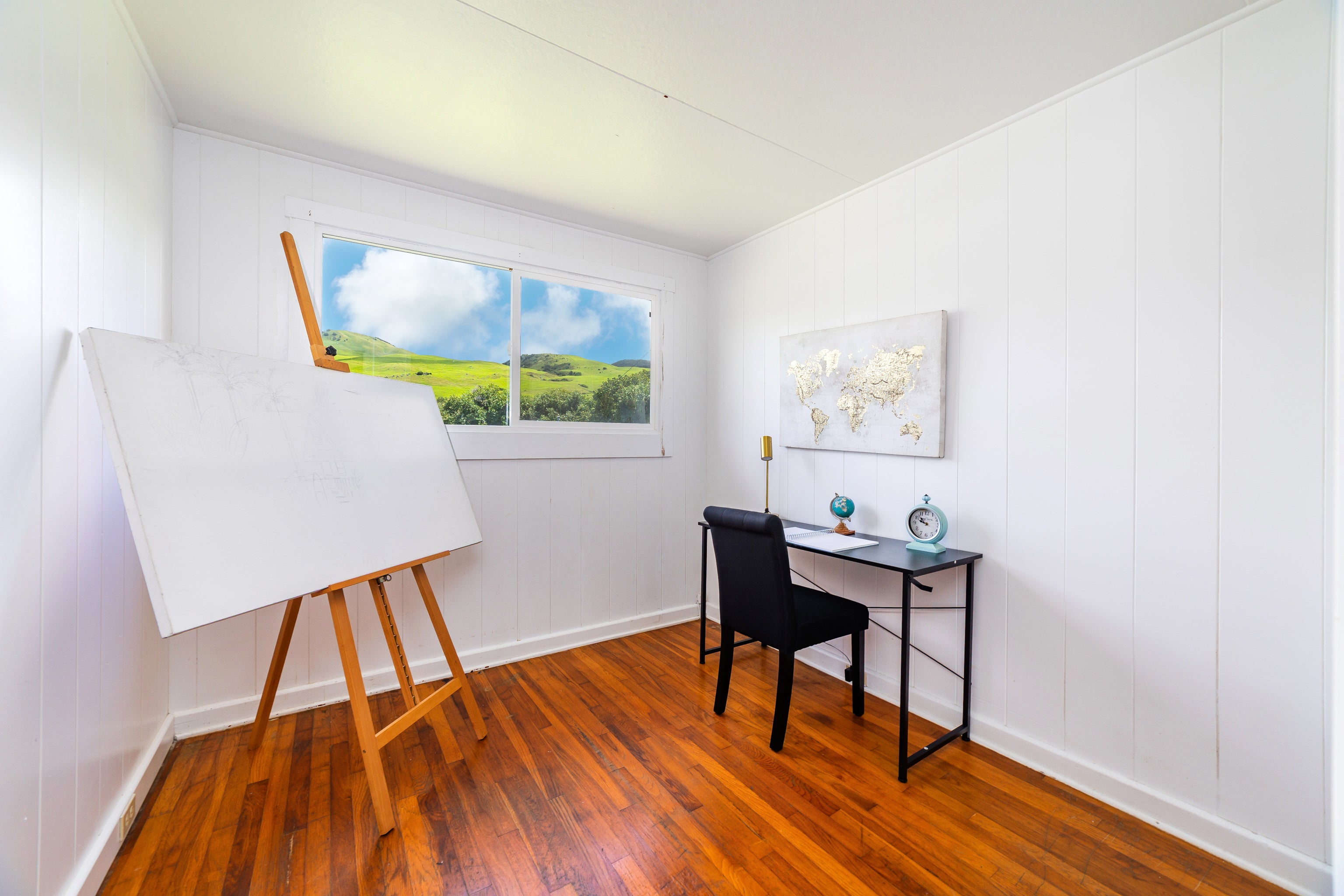 Home office with a large easel whiteboard, black desk, and window overlooking green hills.