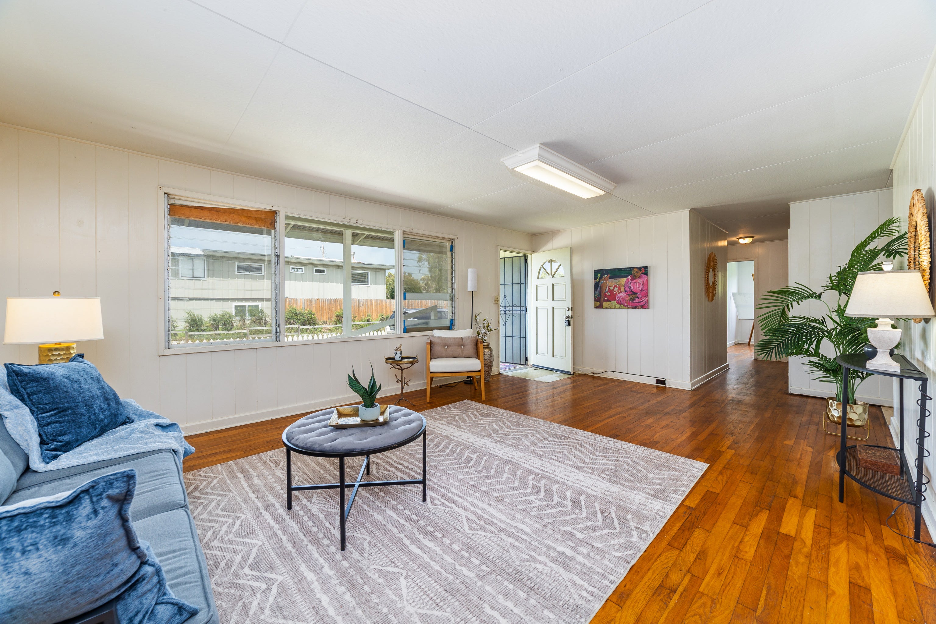 Living room with hardwood floors, a blue sofa, broad windows, and an open front door.