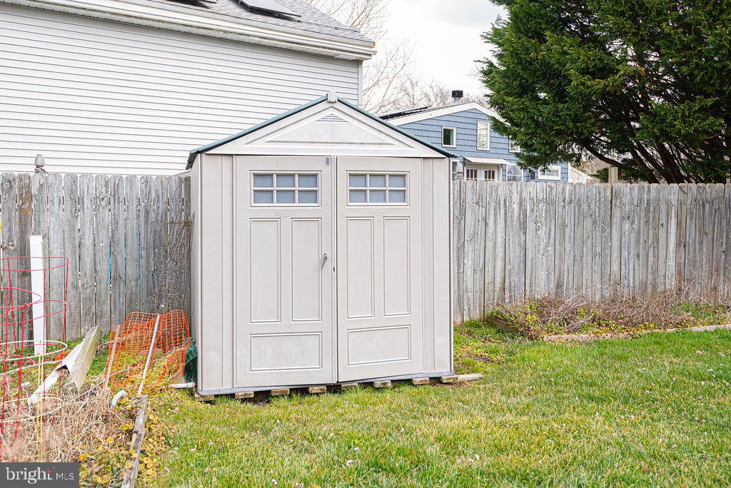 White storage shed with double doors in a fenced backyard.