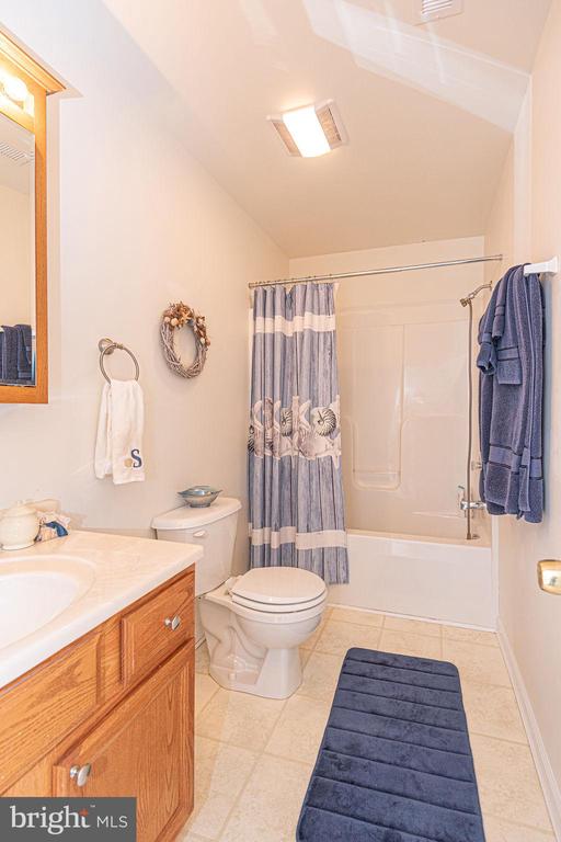 Bathroom with a wood vanity, toilet, and bathtub behind a blue patterned shower curtain.