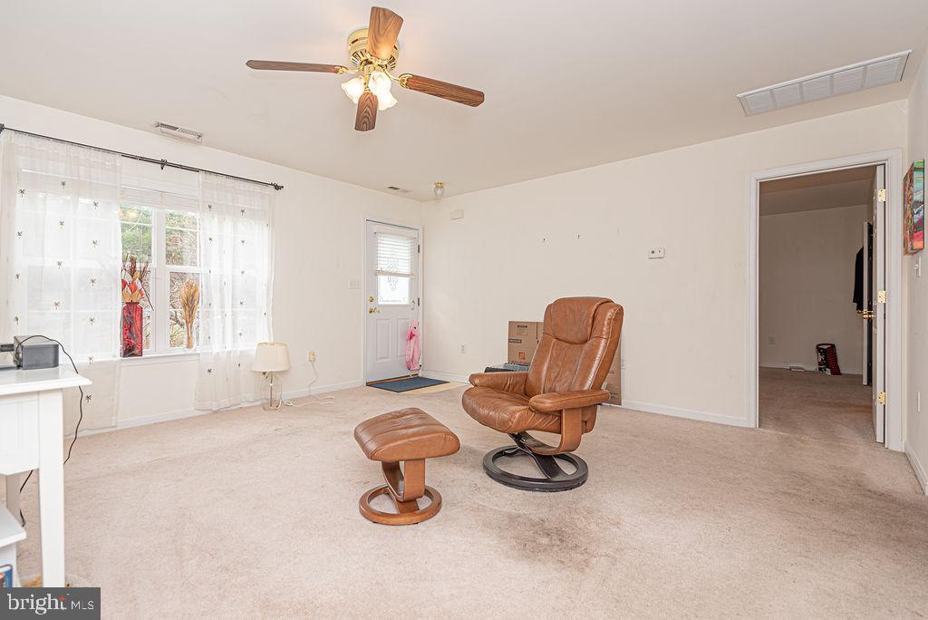 Living room with a brown leather recliner and ottoman, carpet, ceiling fan, and curtained window.