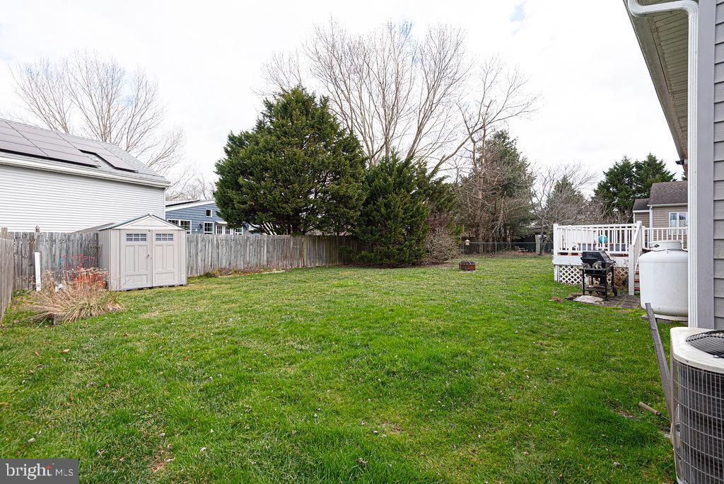 Fenced backyard with a broad lawn, small shed, mature trees, and a raised deck.