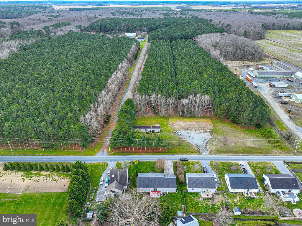 Aerial view of a wooded property with a small building and cleared ground beside a road.