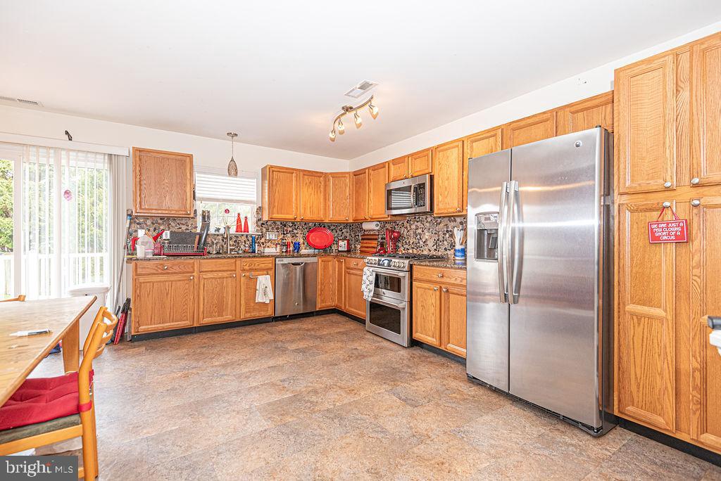 Kitchen with honey-colored cabinets, stainless steel appliances, dark countertops, and a dining table by the sliding door.