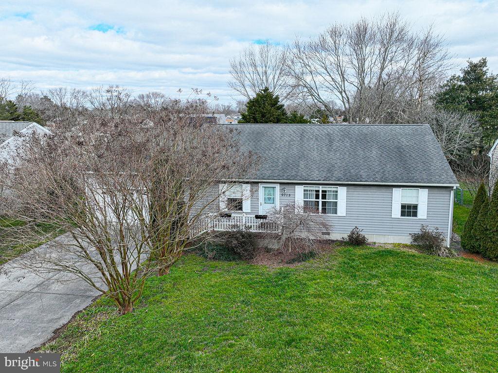 Gray single-story home with a covered porch, broad lawn, and leafless trees partly obscuring the front.