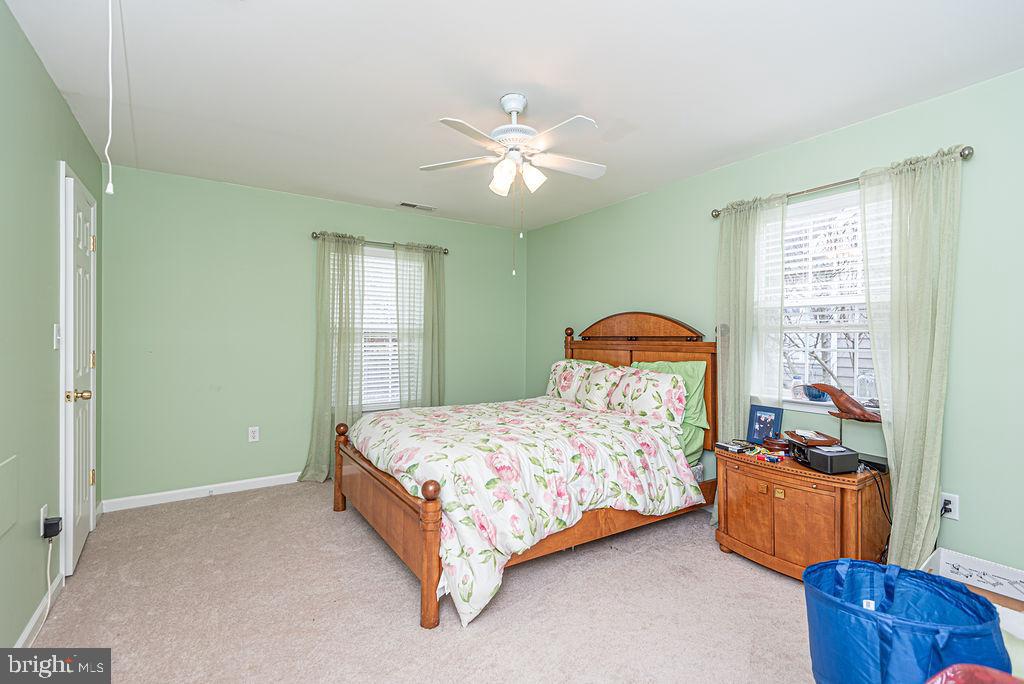 Bedroom with a wooden bed, floral bedding, pale green walls, and two curtained windows.