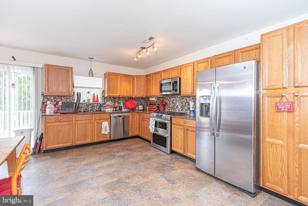 Kitchen with honey-toned cabinets, stainless steel appliances, and a stone-pattern backsplash.