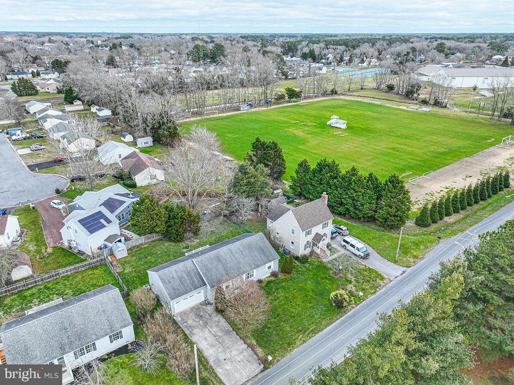 Aerial view of homes beside a large green sports field and tree-lined road.