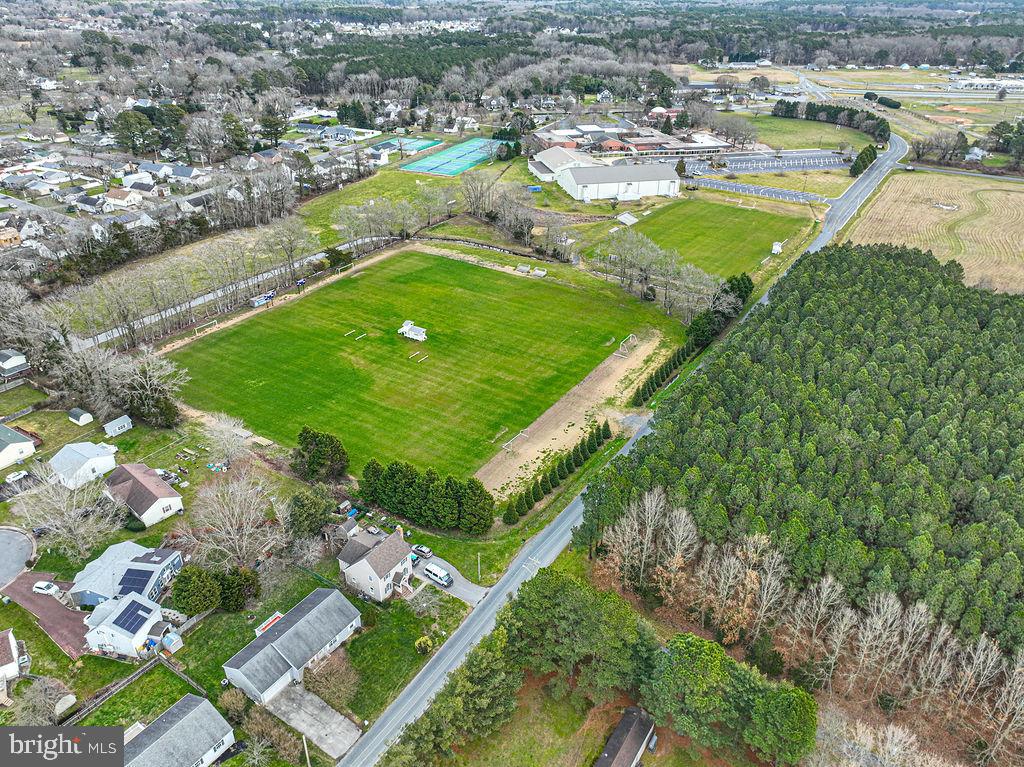 Aerial view of a large green sports field beside homes and wooded land.