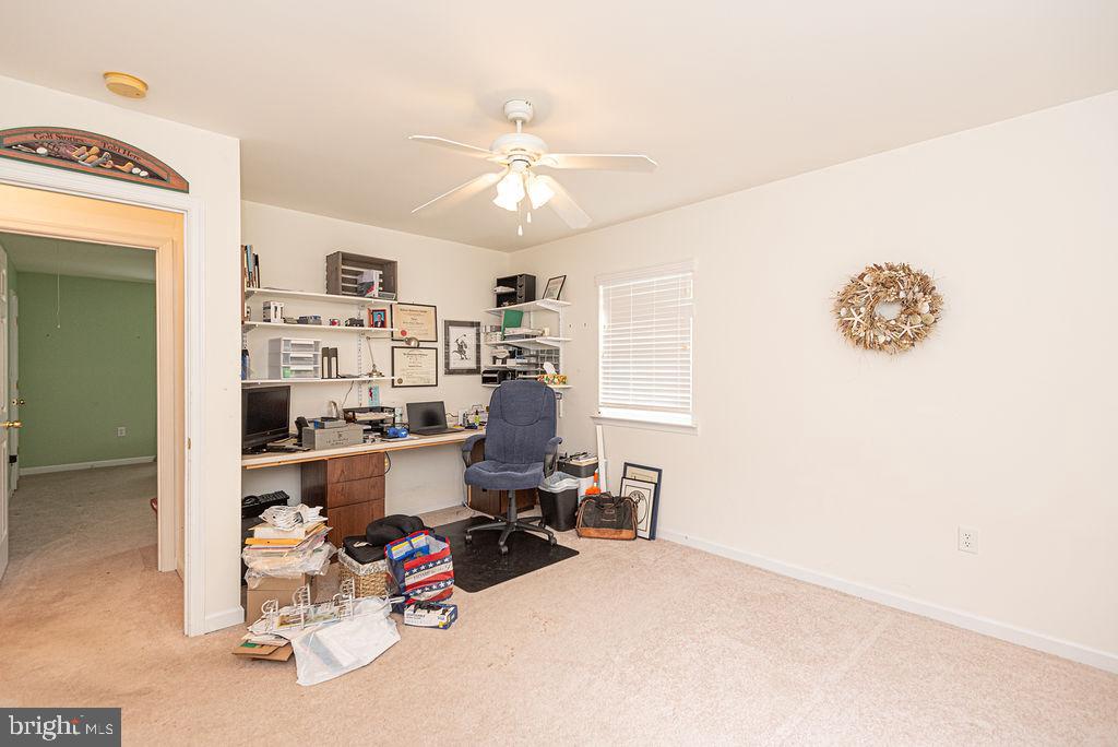 Home office with a crowded desk and shelving beside an open doorway.