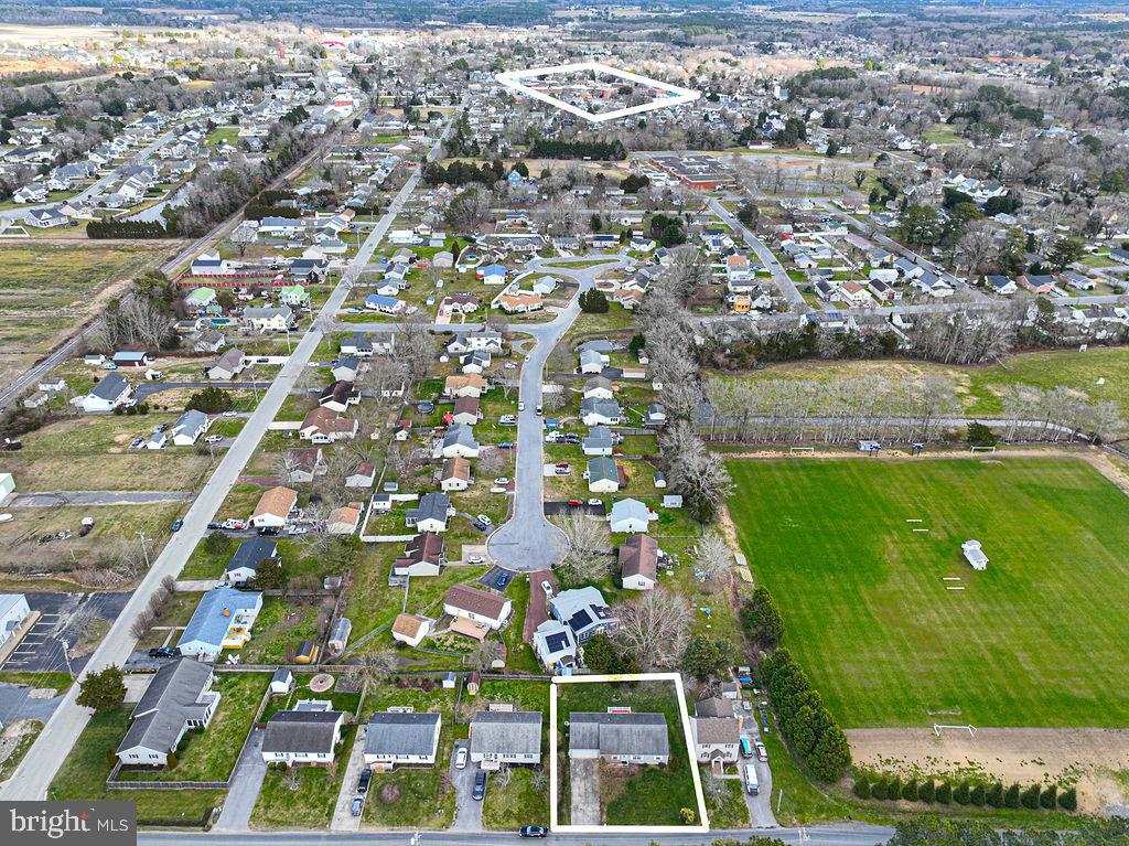 Aerial neighborhood view showing the outlined property lot beside a large green sports field.