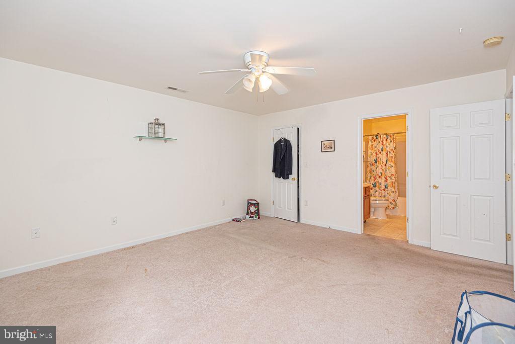 Empty carpeted bedroom with a ceiling fan and an open doorway to a bathroom.
