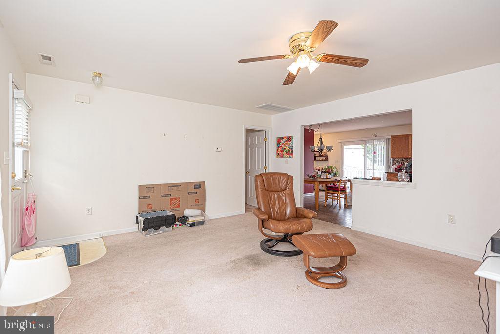 Living room with beige carpeting, a leather recliner and ottoman, and a ceiling fan.