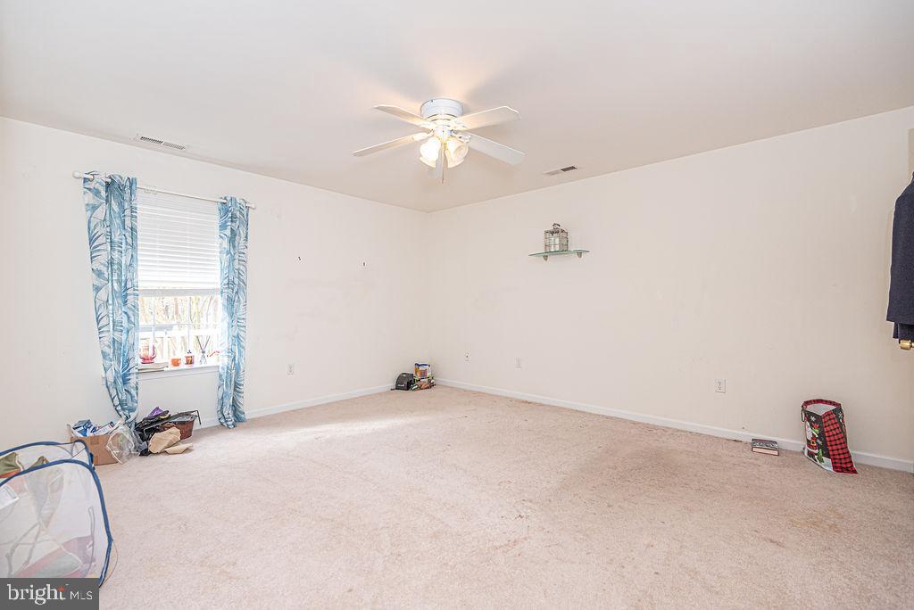 Carpeted bedroom with blue patterned curtains, a ceiling fan, and a small wall shelf.
