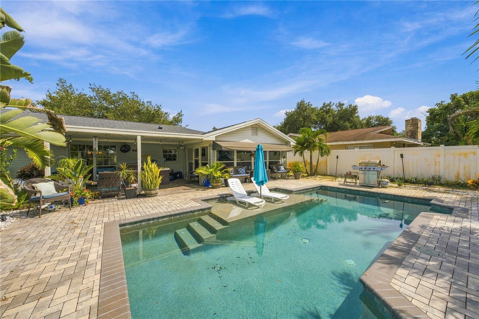 Backyard swimming pool with submerged steps, white loungers, and a covered patio.