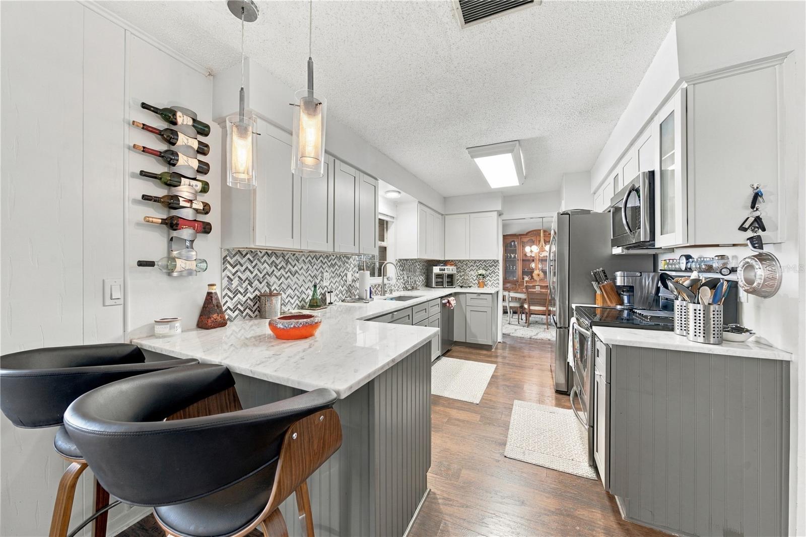 Kitchen with gray cabinets, chevron backsplash, stainless appliances, and a breakfast island with black chairs.