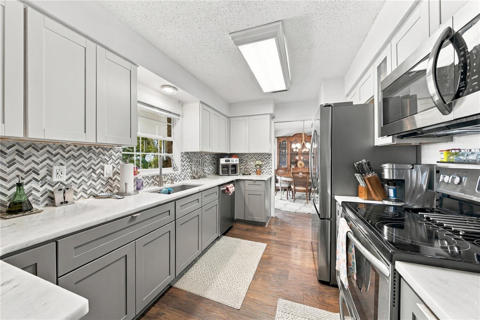 Remodeled galley kitchen with gray cabinets, herringbone backsplash, stainless steel appliances, and dark wood floors.